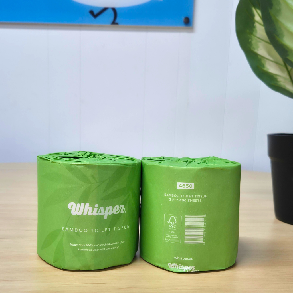 4650 whisper bamboo toilet tissue, toilet paper, made from 100% unbleached bamboo pulp, 2ply, green paper wrapper with leaf shadows, on table, plant in background, black sign