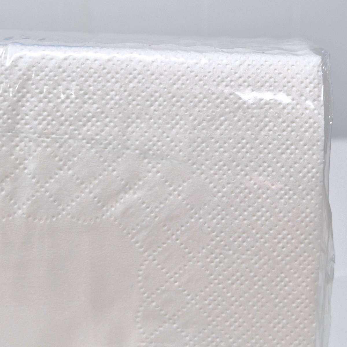 A pack of Whisper brand 2-ply white luncheon napkins in a clear plastic wrapper with a green label showing white cutlery icons and product details. Dot embossing and QT fold.