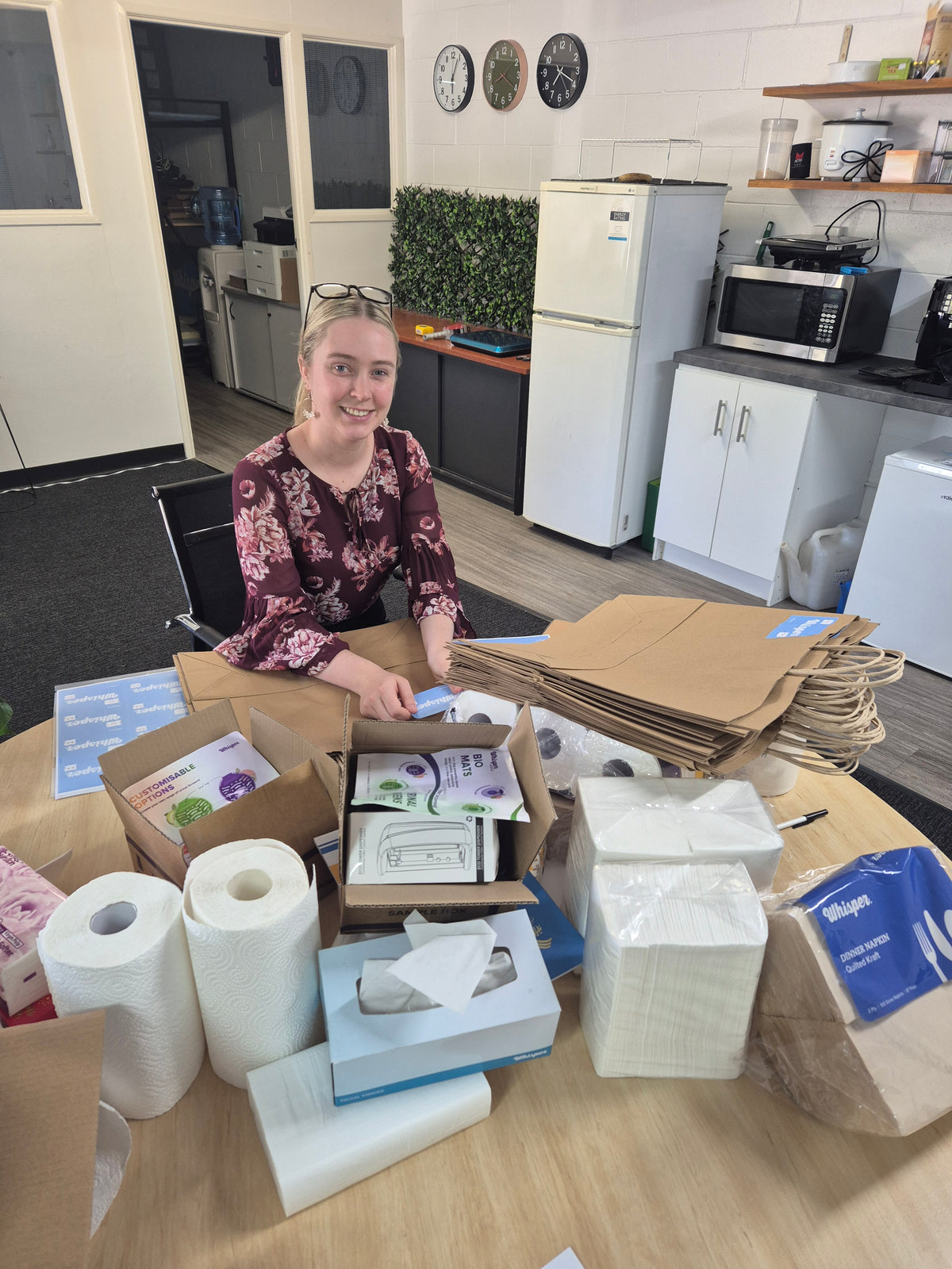 Emily from marketing getting bags ready for trade show, putting whisper stickers on brown paper bags, whisper products in the front on a table