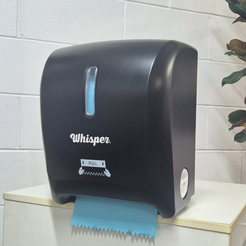 MK8015, Whisper Autocut dispenser, black, white whisper logo, blue paper, roll hand paper towel, white brick background, plant in background, on white table