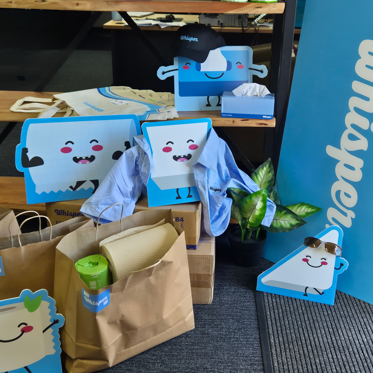 Whisper Characters packing up for a trade show, wearing whisper hats, whisper shirts and sunnies, bags of samples